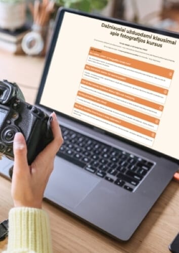 Dažniausiai užduodami klausimai apie fotografijos kursus rodomi kompiuteryje, fotografas rankoje laiko fotoaparatą
