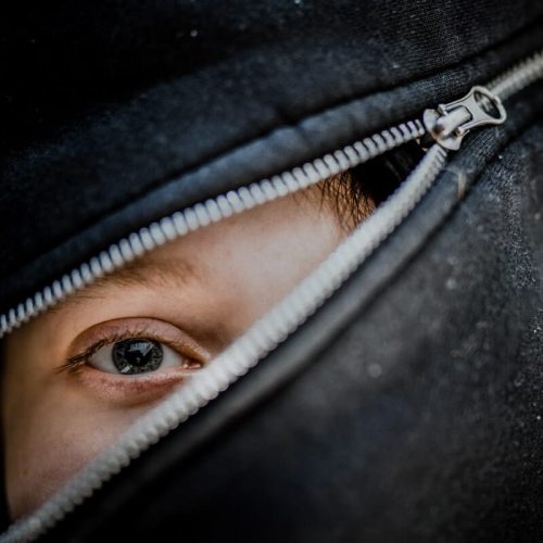 Stambiu planu vienintelė akis tarp užtrauktuku suspausto gobtuvo – fotografijos kursų užduotis 5B, mokinys Robertas B.